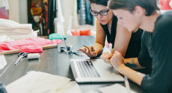 Two people stand over a laptop