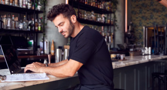 Ein junger Gastronom steht an der Theke seines Restaurants und überlegt sich Marketingstrategien