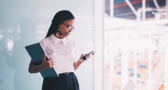 Eine Frau mit Laptop in der einen und Smartphone in der anderen Hand, sieht sich ihre mobile Website auf ihrem Handy an.