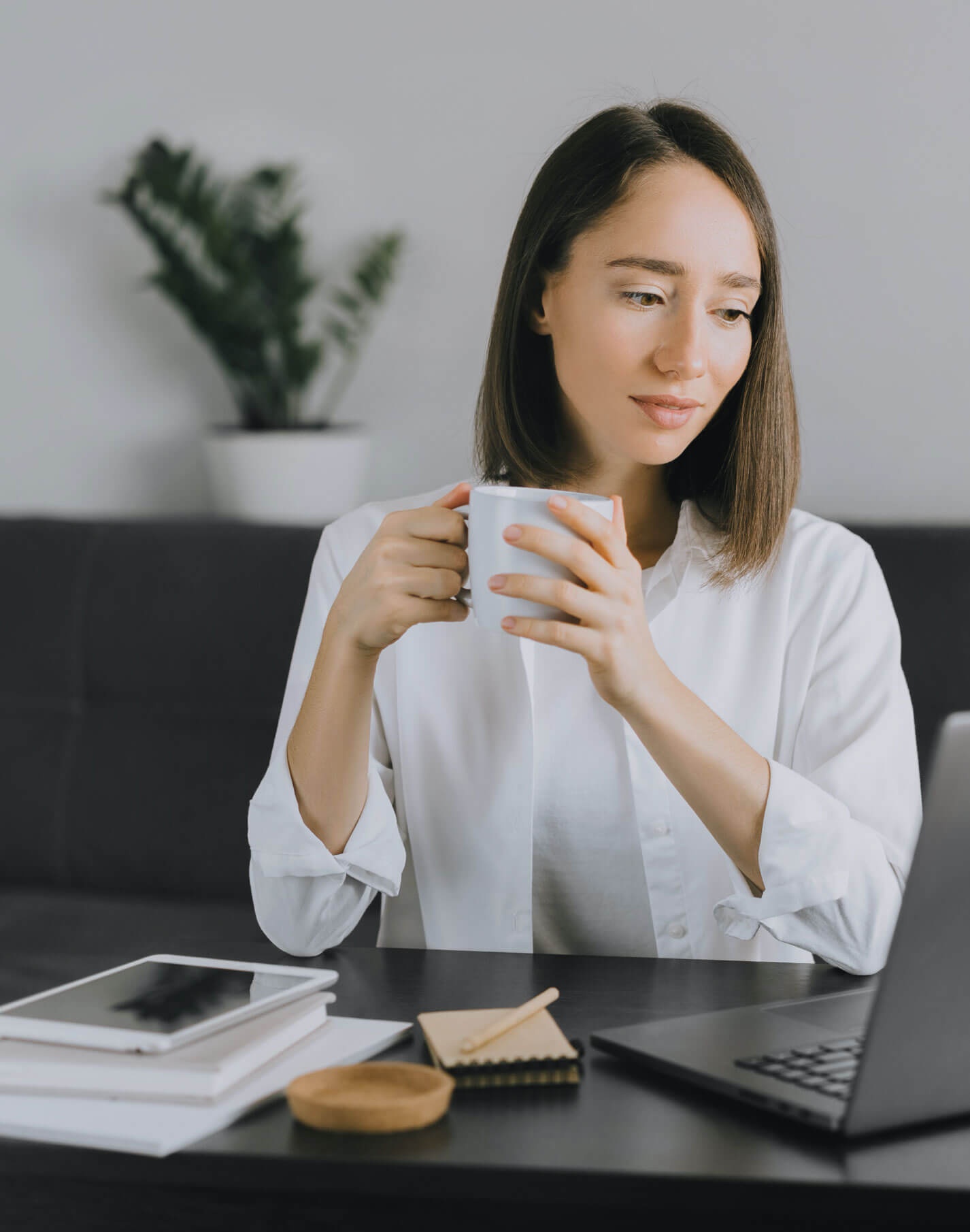 Una mujer toma café y echa un vistazo a la página web de su currículum en su portátil.