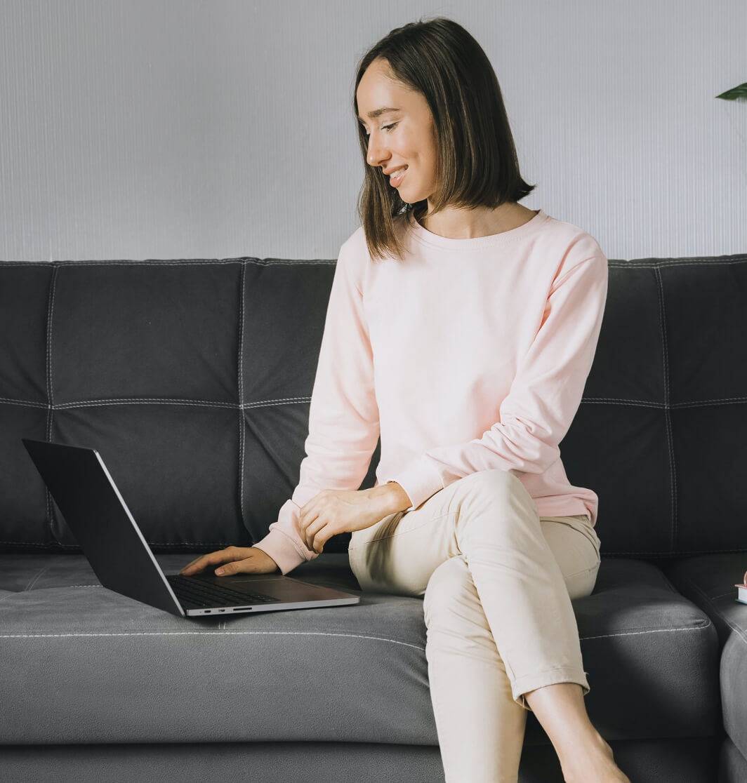 A woman sits on a couch and works on her resume website on her laptop.